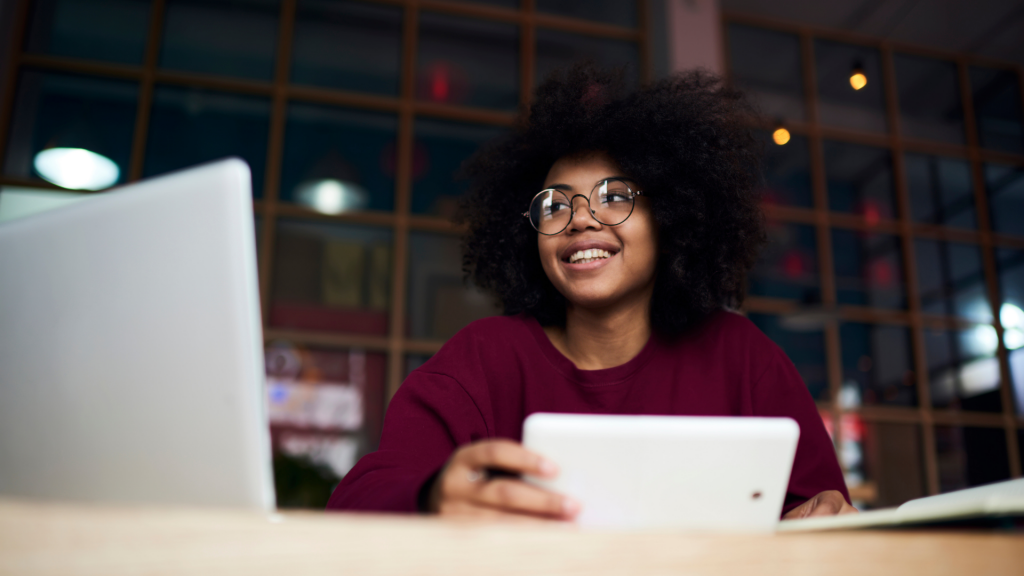 focus on woman at desk with computer and papers, smiling